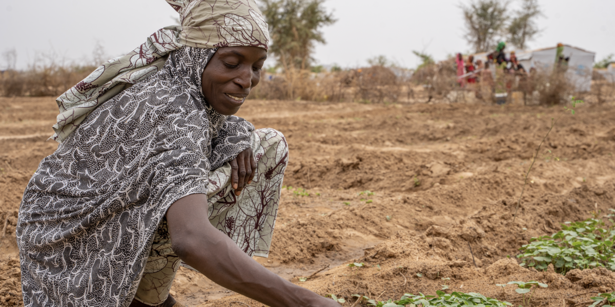 A refugee woman tending to plants in a field while smiling.